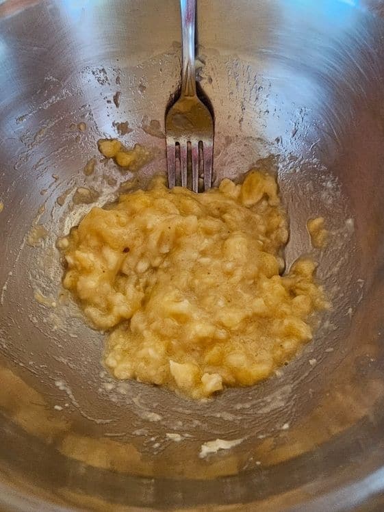 Mashed banana in a mixing bowl with a fork.
