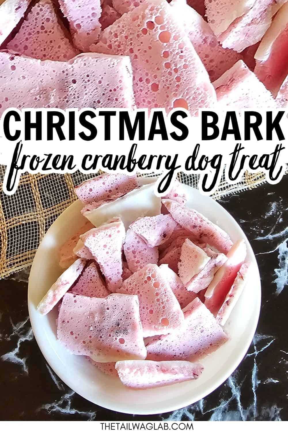 A bowl of frozen cranberry dog treats, labeled as "Christmas Bark," is displayed on a marble surface, showcasing a colorful assortment of treat pieces ideal for holiday gifting to pets.