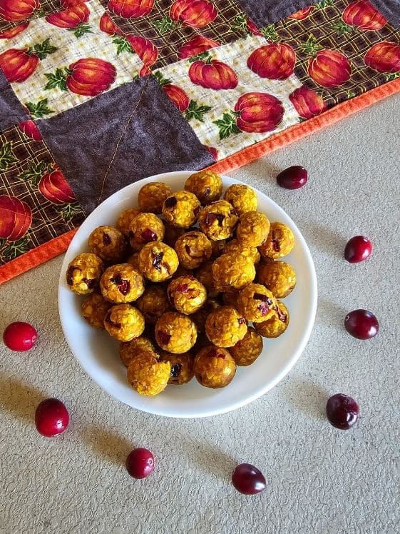 Cranberry oat balls in a white bowl with cranberries around it.