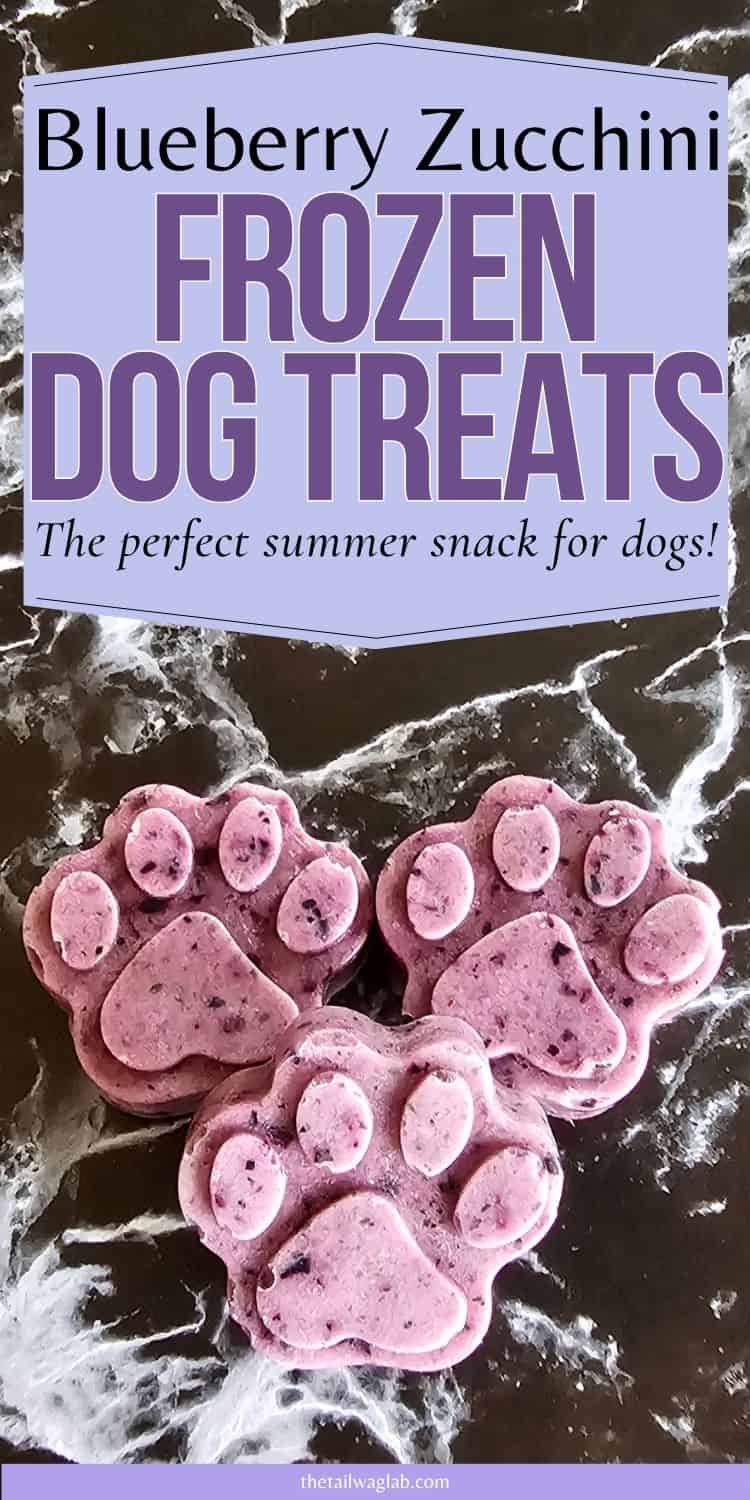 Three frozen dog treats shaped like paw prints are displayed on a marble surface, featuring a blueberry zucchini mixture, labeled as "Frozen Dog Treats" and presented as a perfect summer snack for dogs.