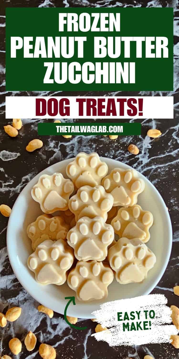 A plate of frozen peanut butter and zucchini dog treats shaped like paw prints is displayed on a marbled surface, accompanied by scattered peanuts.