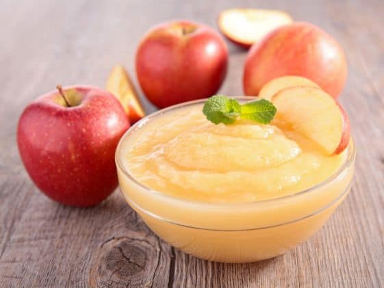 A bowl of applesauce surrounded by apples.
