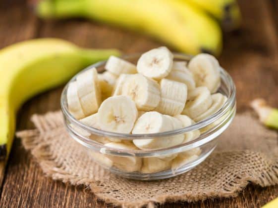 Sliced bananas in a bowl next to a couple of whole bananas.
