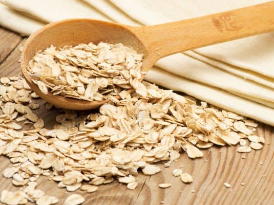 Raw oatmeal oats in a wooden spoon and bowl.