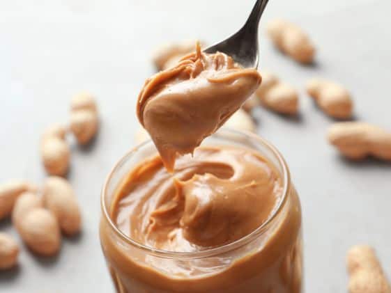 Creamy peanut butter on a spoon above a jar of peanut butter.