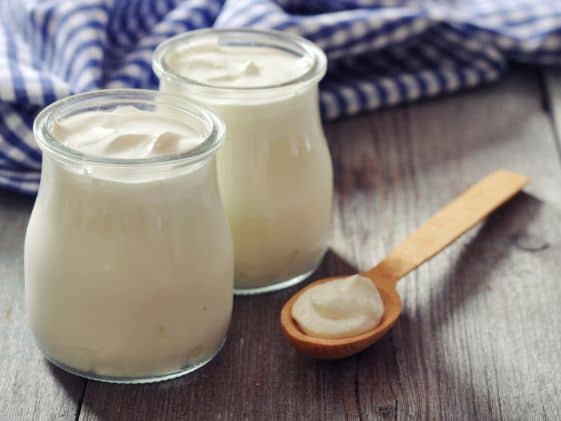 Two glass jars of Greek yogurt next to a wooden spoon.