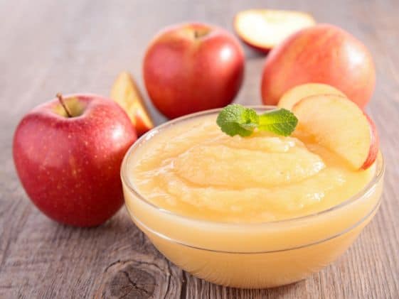 A bowl of applesauce next to some apples.