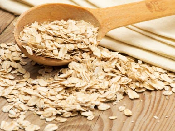 Raw oats spilled from a wooden spoon on a wooden surface.