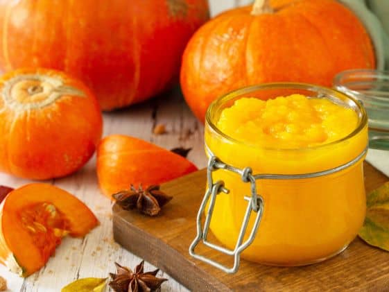 Fresh pumpkin puree in a jar with pumpkins and spices around it.