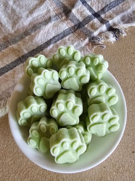 A bowl of paw shaped cucumber mint frozen dog treats next to a linen towel.