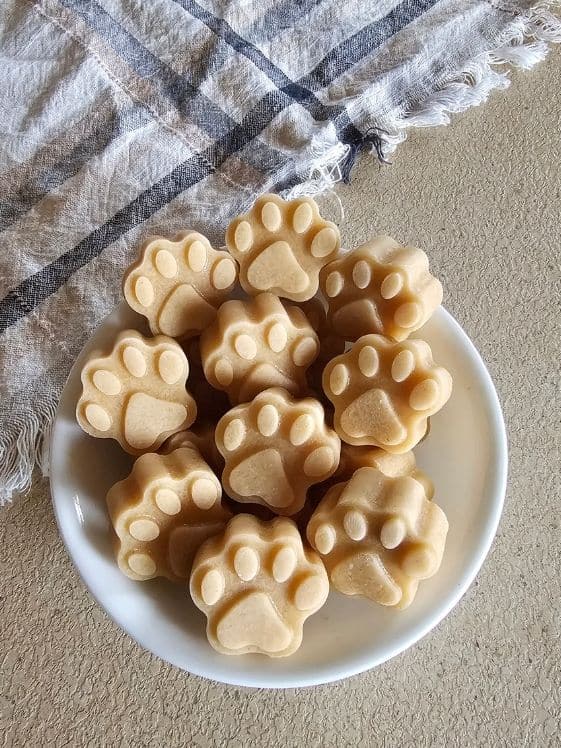 A bowl of paw shaped frozen peanut butter applesauce dog treats next to a linen towel.