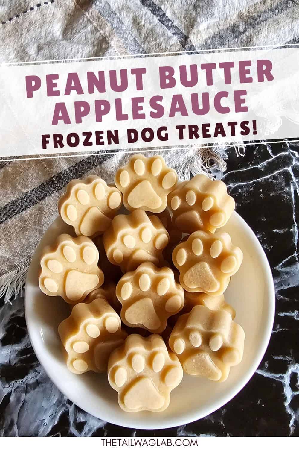 A bowl of frozen peanut butter applesauce dog treats shaped like paw prints with text that reads "Peanut Butter Applesauce Frozen Dog Treats." Homemade frozen treats that are easy to make and freezer-friendly.