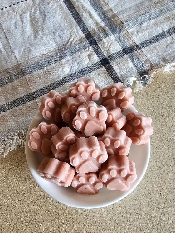 A bowl of paw shaped cucumber watermelon mint frozen dog treats next to a linen towel.