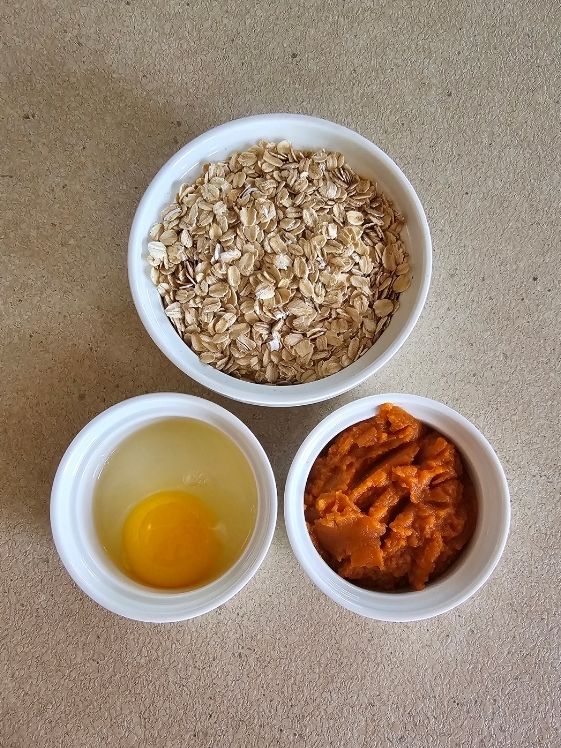 Oats, pumpkin puree, and an egg in individual white bowls.